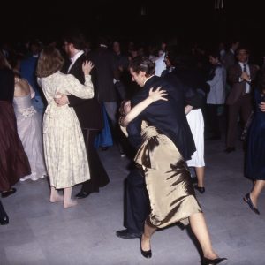 A candid photo of a waltz at Grinnell in 1986. A couple is centered in the image, and the man is in the midst of dipping his partner. Other couples surround them, and everyone is in semi-formal wear such as suits and mid-length dresses.